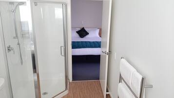Une chambre d’hôtel avec une douche, un lit recouvert d’une couette bleue et blanche, et une serviette blanche posée sur un porte-serviettes en métal.