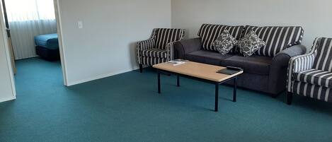 Un salon avec un canapé, deux fauteuils à rayures, une table basse et un tapis bleu.