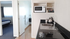 A hotel room with a bed, a bathroom with a shower, and a kitchenette with a microwave and kettle. - Central Motor Lodge (Morrinsville)