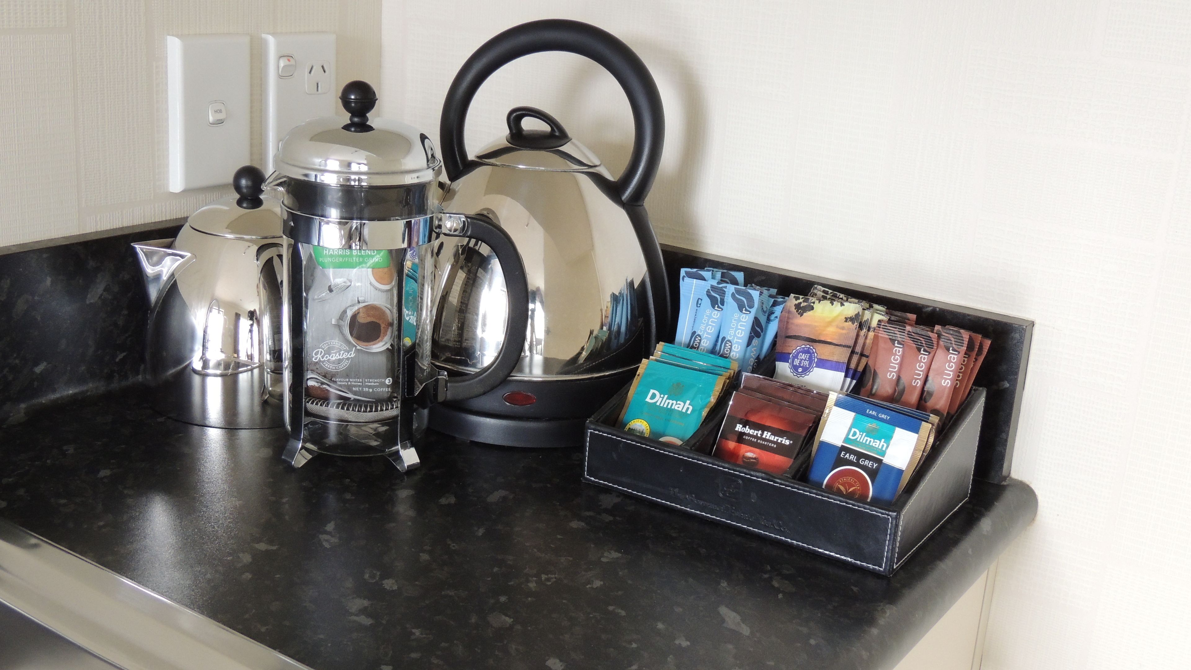A kitchen counter with a coffee maker, a kettle, and a box of coffee pods.
