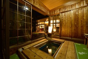 A traditional wooden bathhouse with a wooden interior, a small water feature, and a view of the outside.