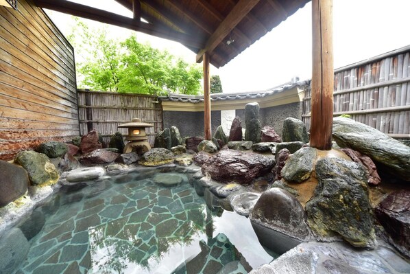 A traditional Japanese onsen with a stone bath surrounded by rocks and a wooden structure.