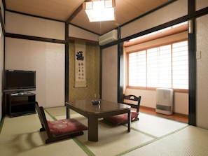 Een traditionele Japanse kamer met tatami vloerbedekking, een lage tafel, een televisie en een schuifdeur.