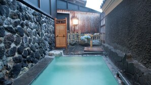 Ein traditionelles japanisches Onsen mit einer Steinsäule, einem Holztor und einem kleinen Garten mit Blumen.