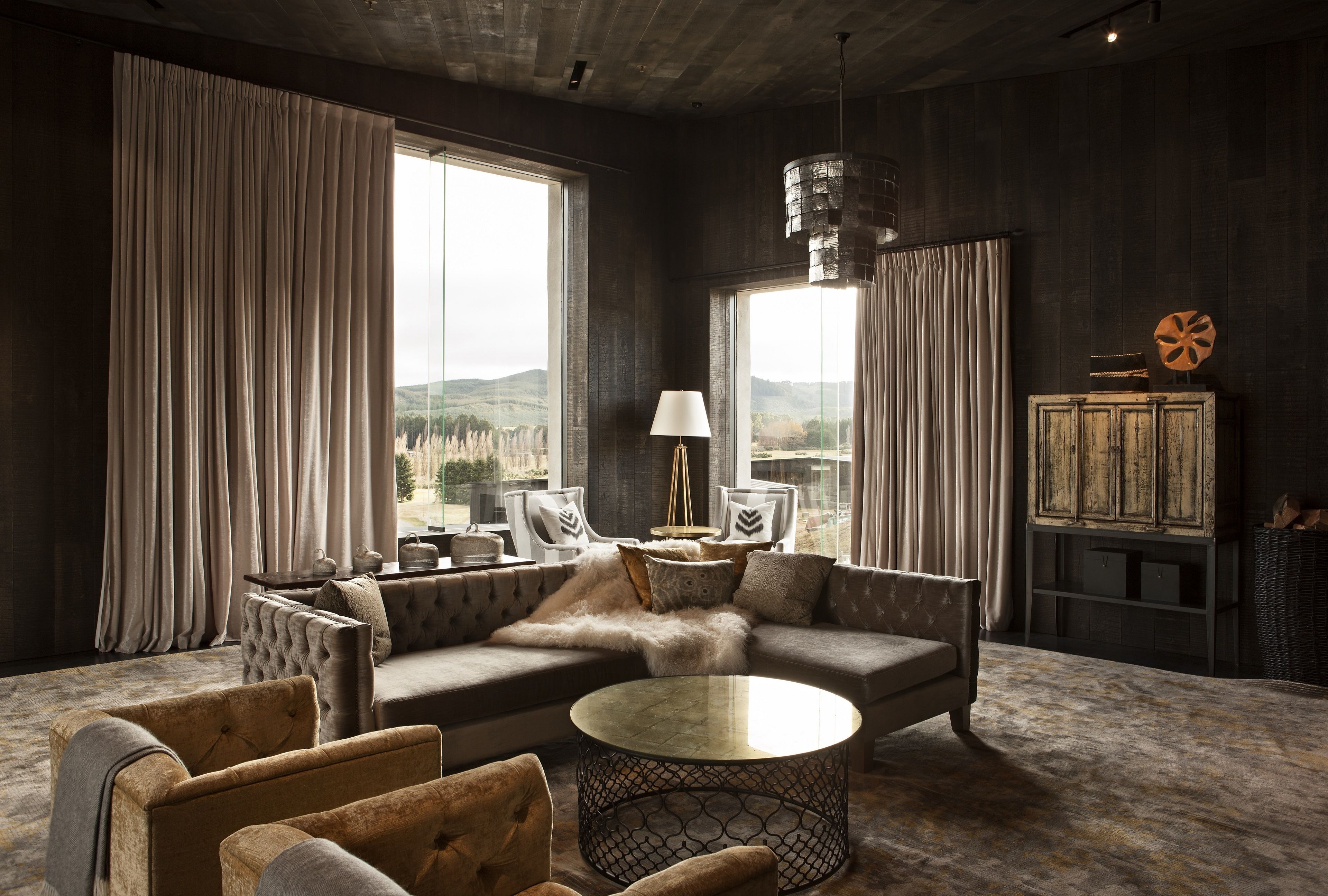 A modern living room with a sectional sofa, armchairs, a round coffee table, and a view of the outdoors through large windows.