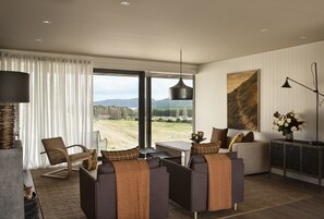 Una sala de estar moderna con un ventanal grande, un conjunto de sofás, una mesa y una lámpara colgante.
