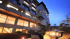 A multi-story hotel with large windows and a stone lantern in the foreground. - Yuruino Yado Keizan (Achi)