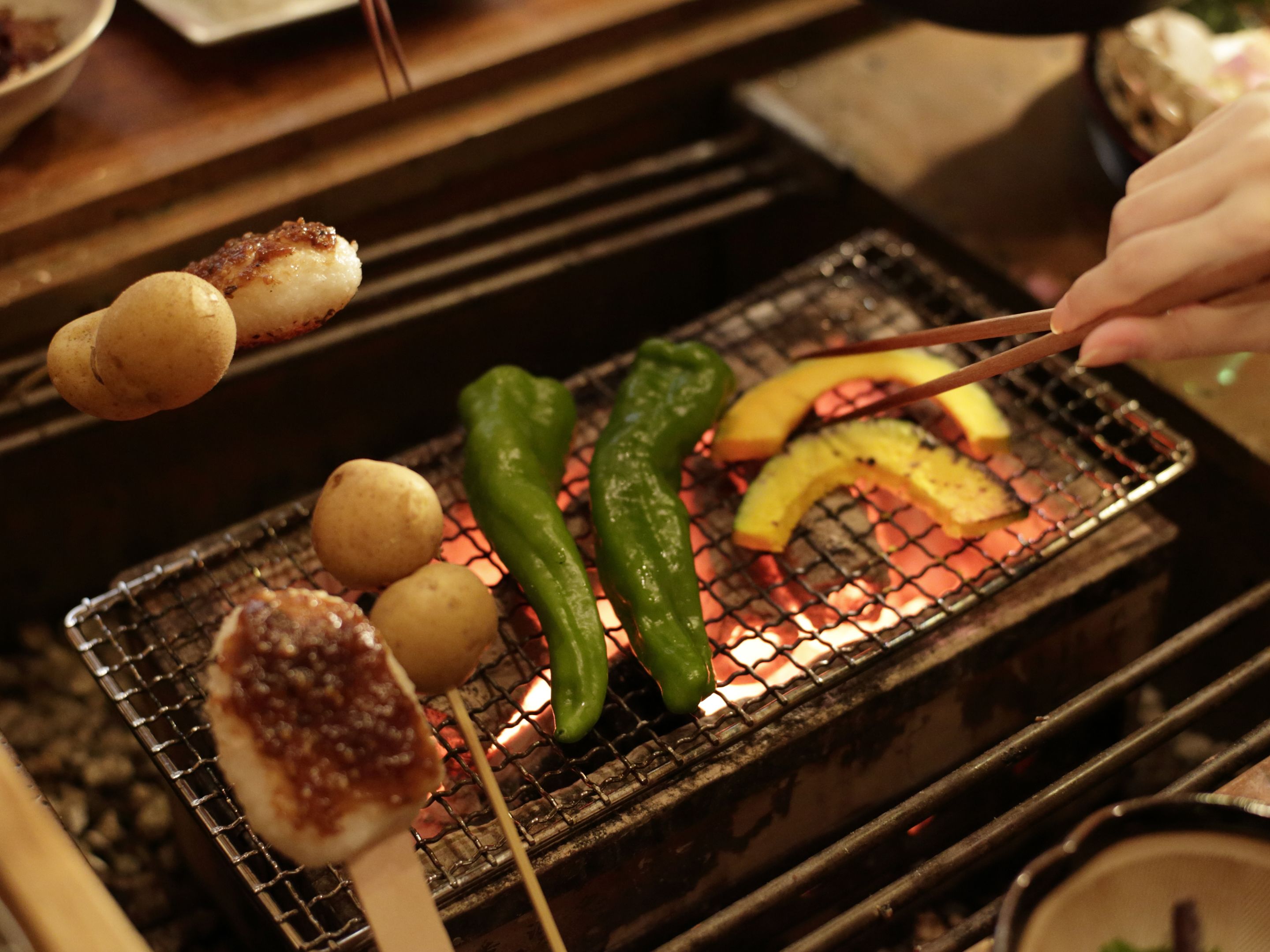 A grill with skewers of food, including potatoes and green peppers, being cooked over an open flame.
