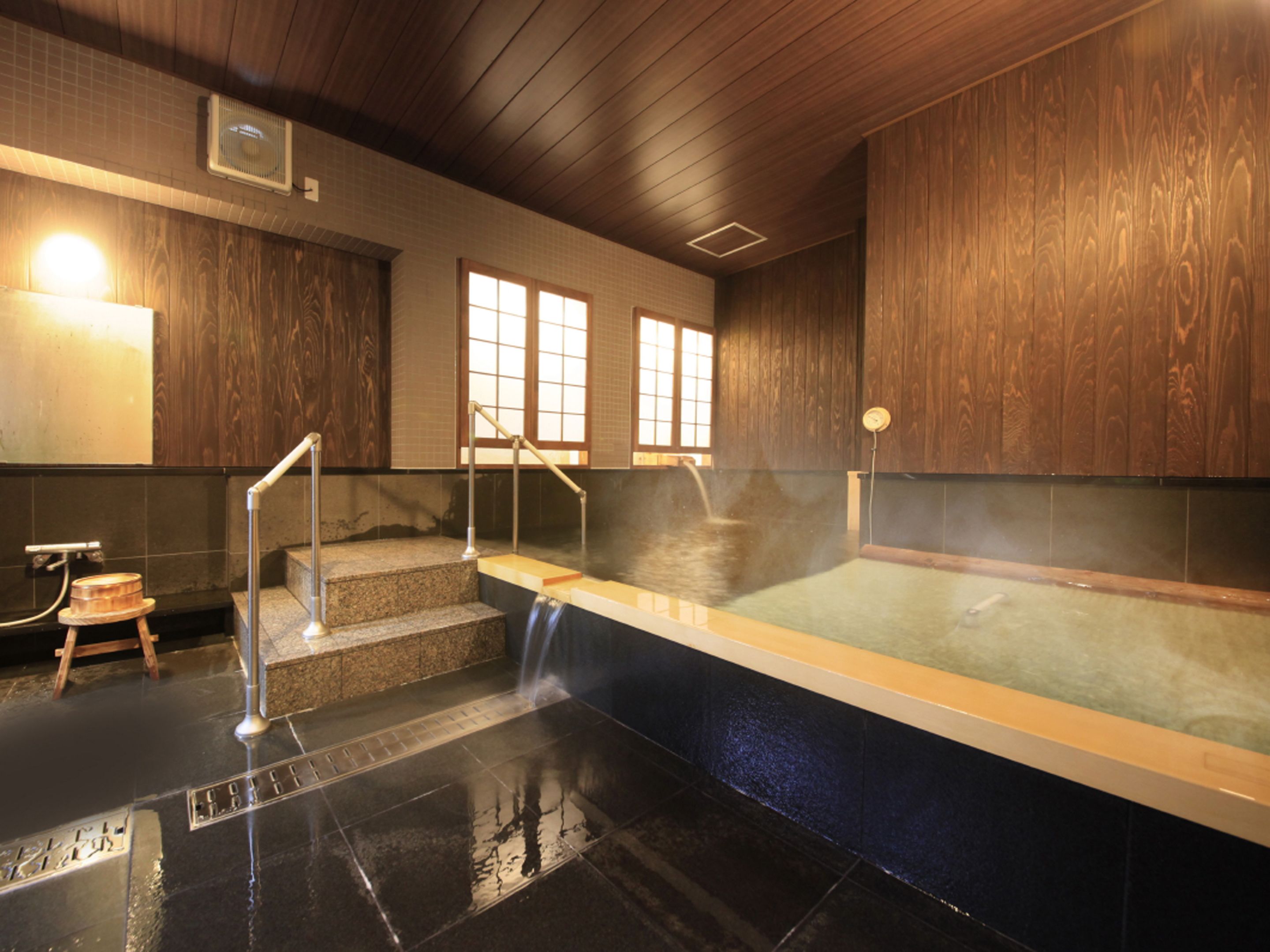 A traditional Japanese onsen with a wooden interior, a stone hot spring, and a small wooden stool.