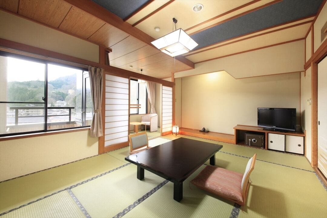 A traditional Japanese room with tatami flooring, a low table, a bench, a television, and a sliding door leading to a balcony.