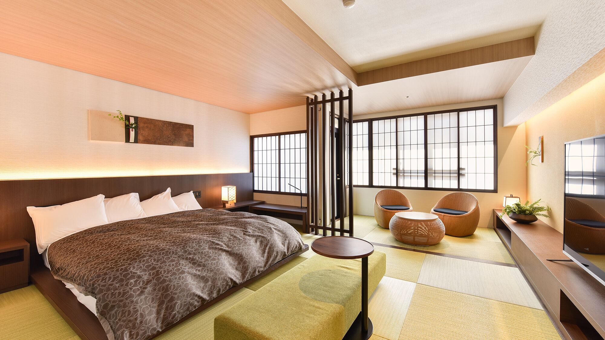 A modern hotel room with a large bed, a small round table, two chairs, a TV, and a view through a shoji screen.