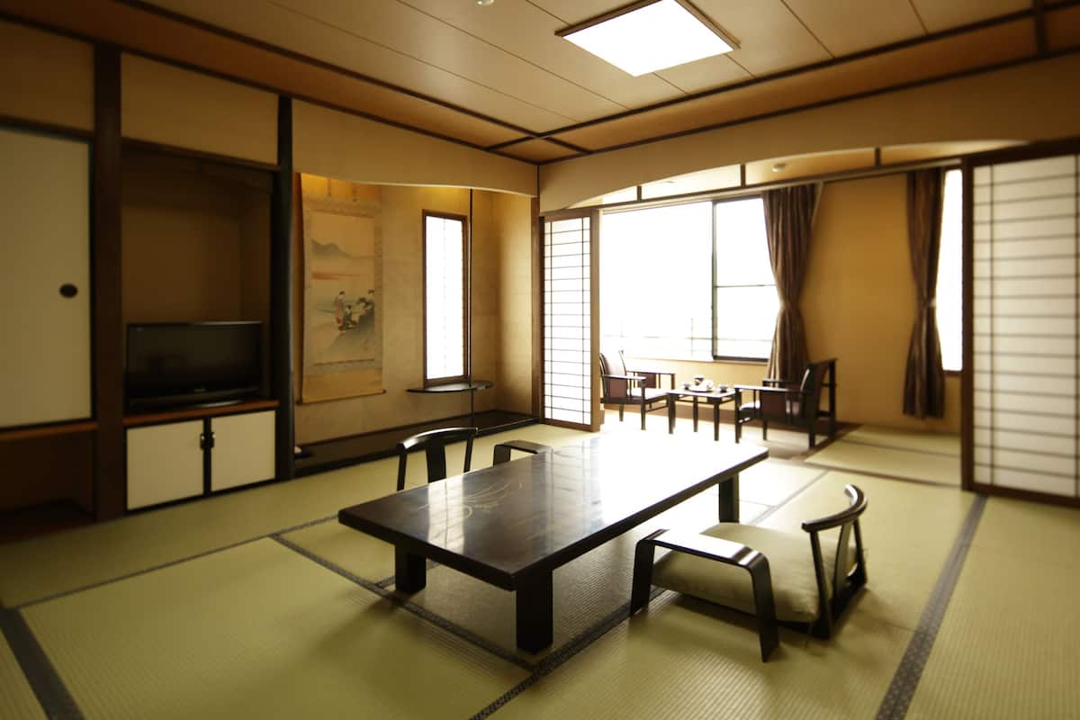 Et traditionelt japansk rum med tatamimåtter, et lavt bord med puder, skydedøre og et fjernsyn på et skab.