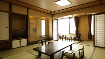A traditional Japanese room with tatami flooring, a low table with cushions, sliding doors, and a television on a cabinet.