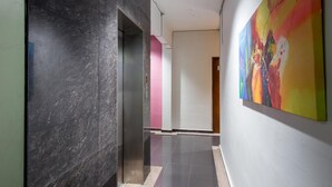A hallway with a marble wall, a colorful abstract painting, and a door in the background.