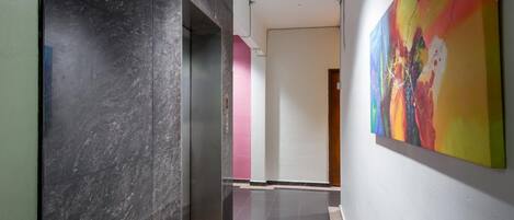A hallway with a marble wall, a colorful abstract painting, and a door in the background.