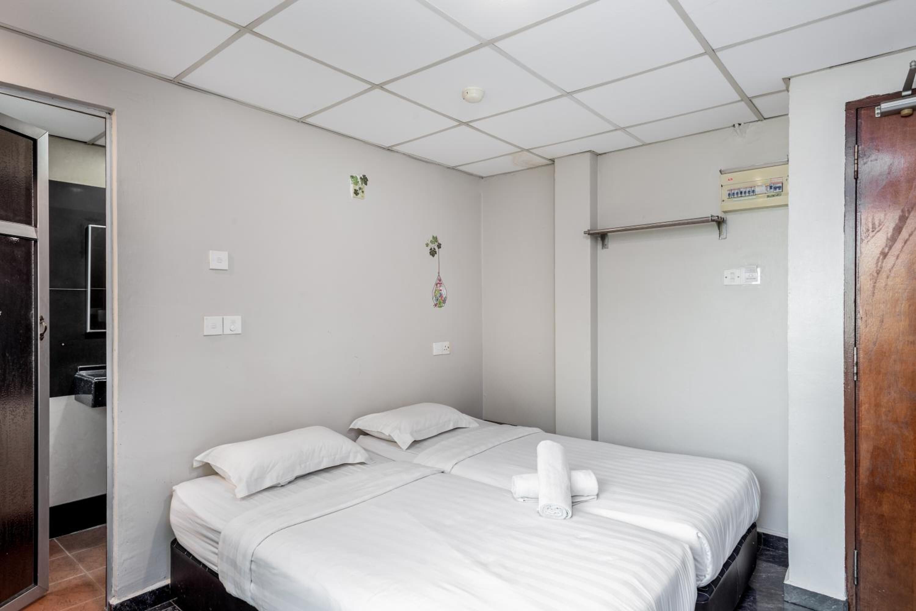 A hotel room with a bed, a wooden door, a towel on the bed, and a wall-mounted air conditioning unit.