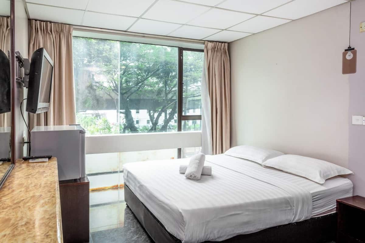A hotel room with a bed, a desk with a chair, a TV, and a window with curtains.
