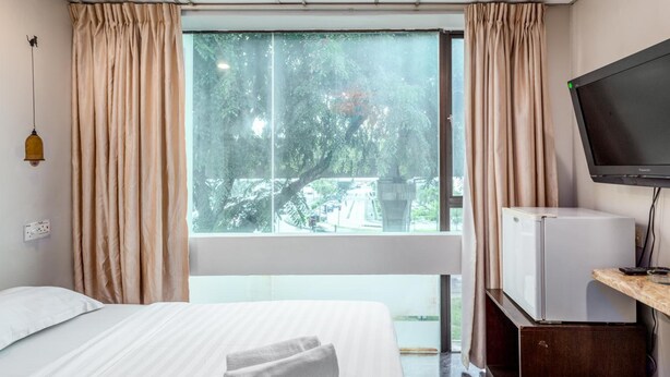 A hotel room with a bed, a television, a small refrigerator, and a window with curtains.