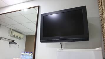 A room with a mounted television, a white refrigerator, and a mirror on the wall.