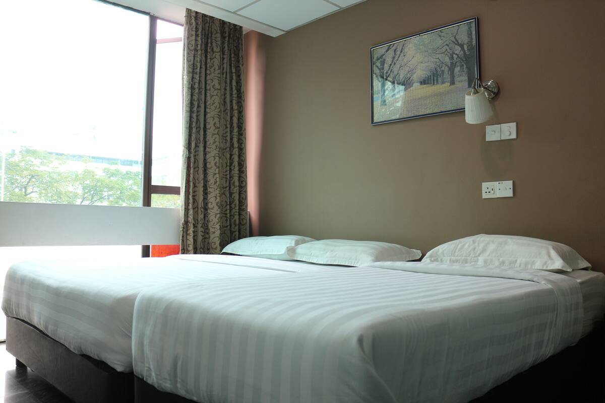 A hotel room with a large bed, a window with curtains, a wall-mounted lamp, and a painting.