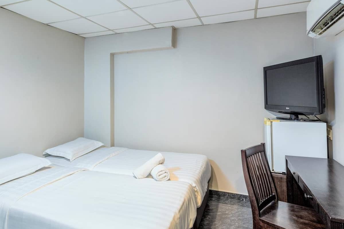 A hotel room with two beds, a desk, a chair, a television, and an air conditioning unit.