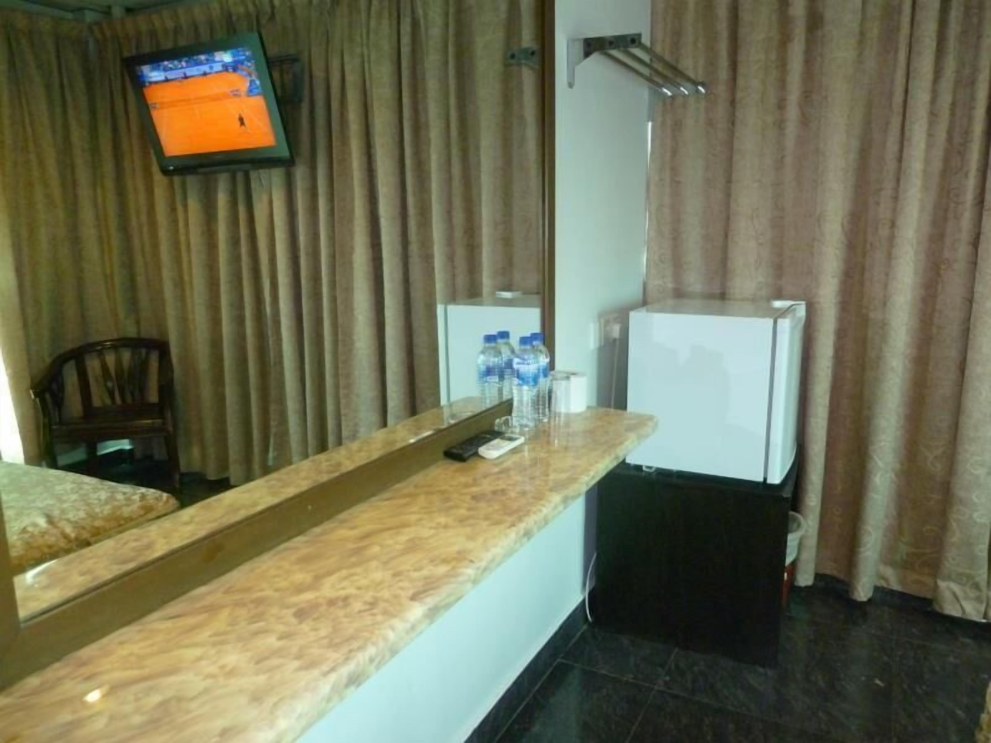 A hotel room with a marble counter, a television mounted on the wall, a small refrigerator, and a chair.