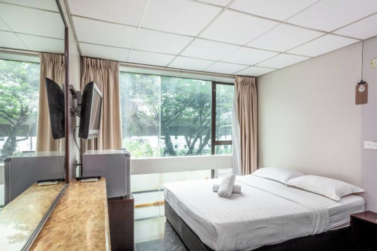 Una habitación de hotel con cama, escritorio, silla, televisor y ventanas amplias.