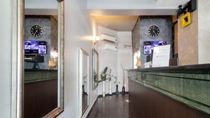A reception area with a dark wood floor, two wall clocks, a flat-screen TV, and a reception desk with a glass top.