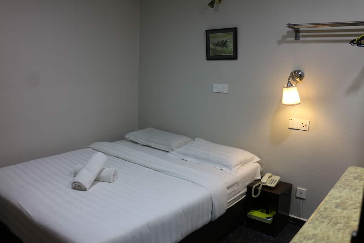 A hotel room with a neatly made bed, a bedside telephone, and a wall-mounted light fixture.