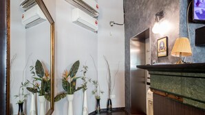 A hotel reception area with a mirror, air conditioning units, a reception desk, and potted plants.
