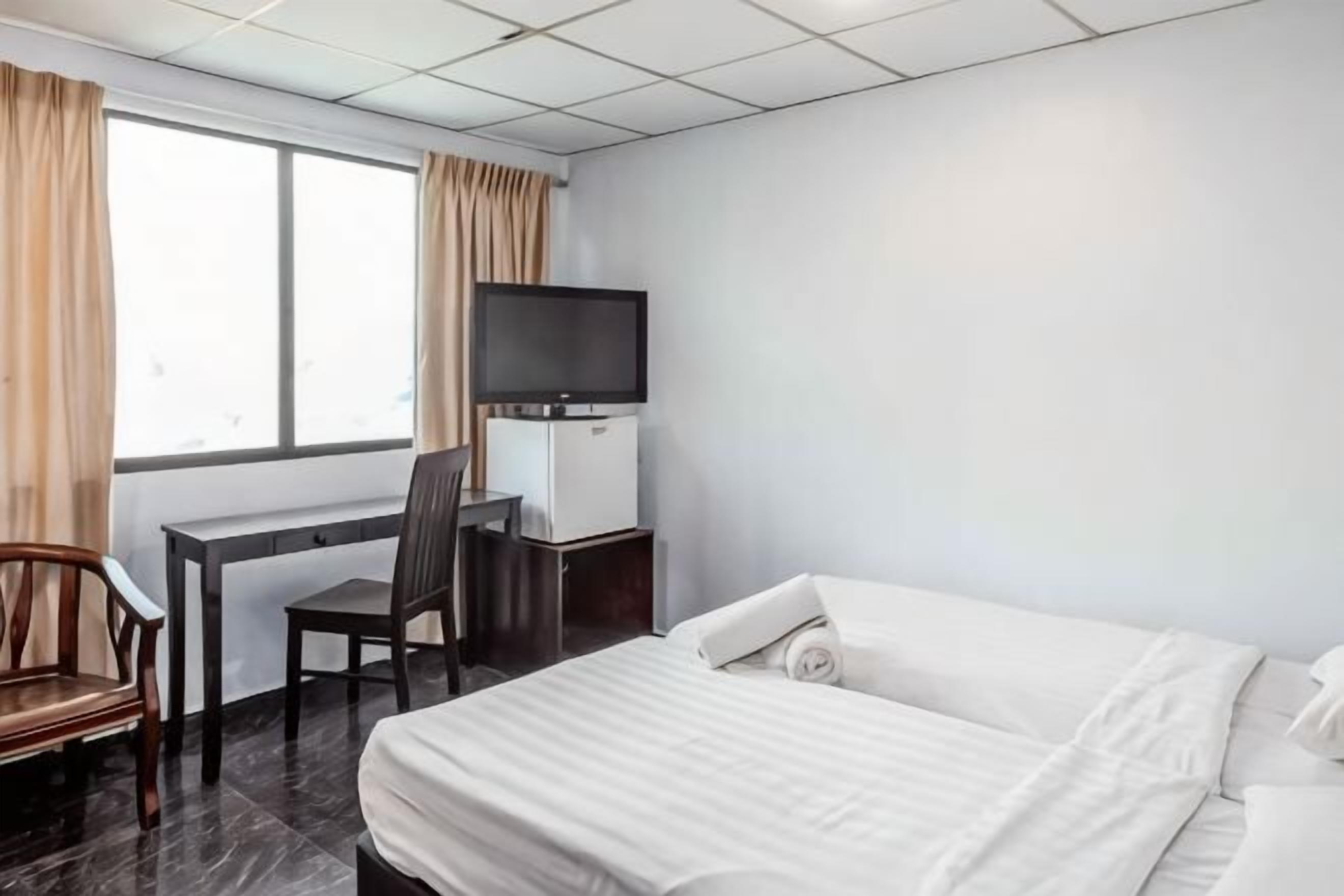 Ett hotellrum med en säng, ett skrivbord med en stol, en tv och ett fönster med gardiner.