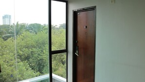 A room with a large window, a wooden door, and a view of greenery outside.