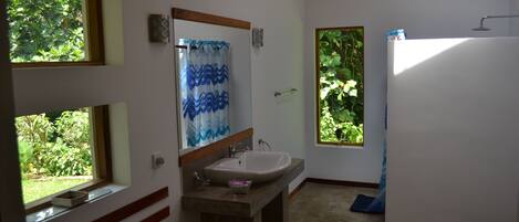 A bathroom with a sink, mirror, and toilet. There are windows providing natural light and views of greenery.
