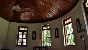 Una habitación con techo de madera alto, ventanas grandes con barrotes y una mesa con un florero.