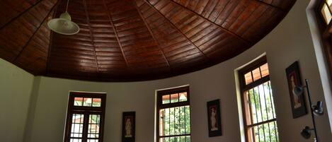 Una habitación con techo de madera alto, ventanas grandes con barrotes y una mesa con un florero.
