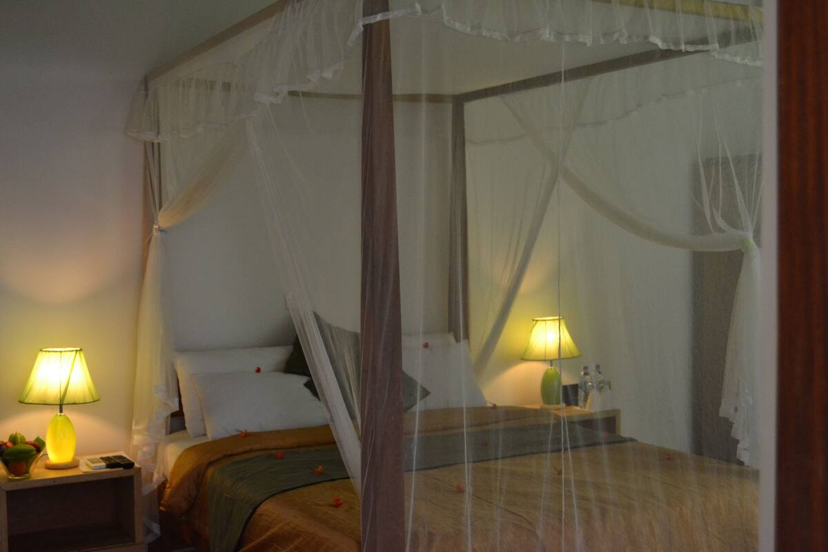 Ein Schlafzimmer mit Himmelbett, zwei Nachttischlampen und einem Nachttisch mit Telefon und kleiner Pflanze.