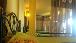 Una habitación con cama, una silla, una mesa y un ventanal con cortinas.