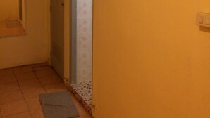 Un pasillo estrecho con suelo de baldosas, una puerta a la izquierda y una pared con toma de corriente a la derecha.