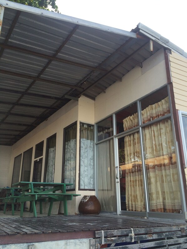 A building with a metal roof, large windows with curtains, and a green bench outside. - Supreeya Guesthouse - Hostel (Ko Pha-ngan)