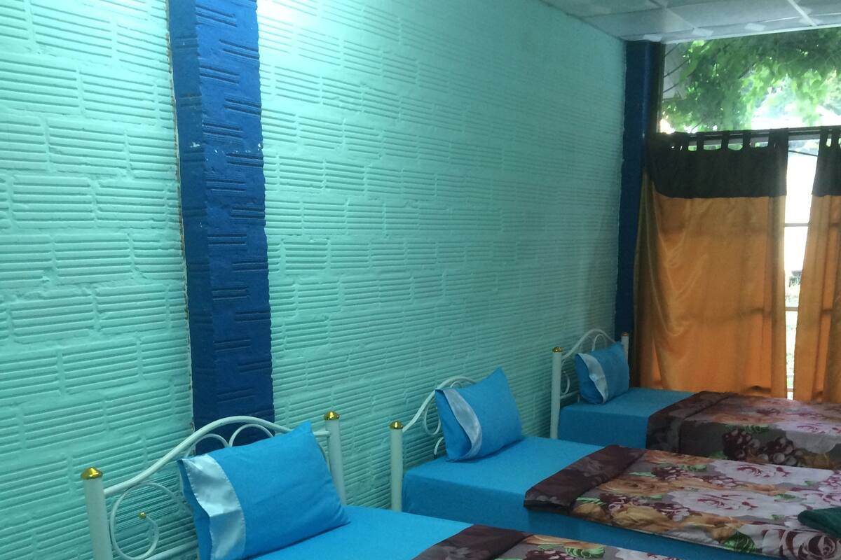 Una habitación con dos camas, cada una con una colcha de flores y ropa de cama azul. Las paredes tienen textura y están pintadas en un tono claro.