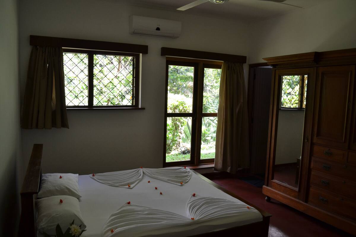 Un dormitorio con cama, dos ventanas, armario y aire acondicionado.