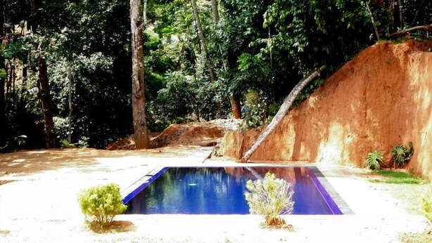 Una piscina rodeada por un paisaje natural con árboles y una colina rocosa.