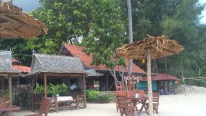 Un restaurante frente a la playa con mobiliario de madera y sombrillas de paja.