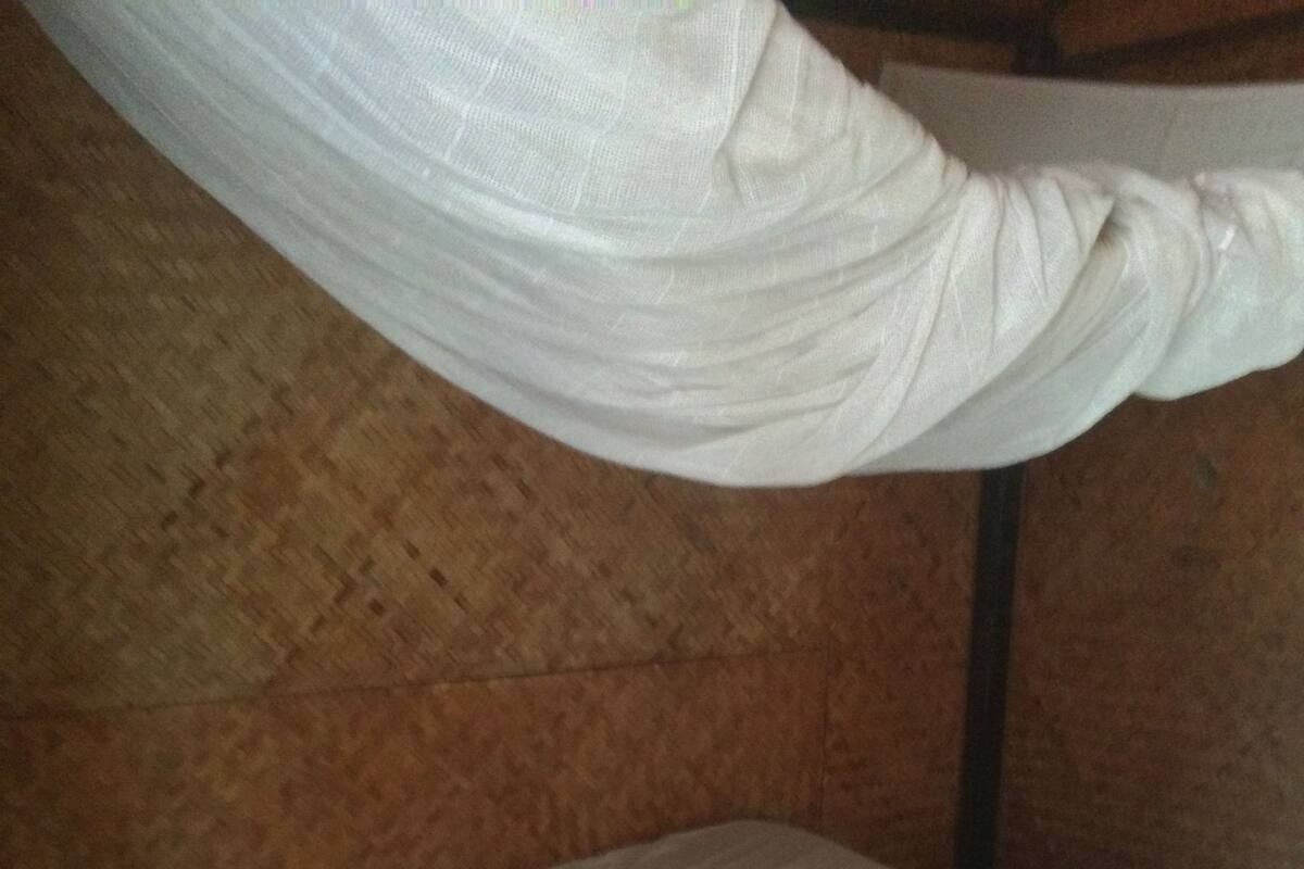 Een eenpersoonsbed met hemelbed, een houten hoofdbord en een matras met een wit laken en twee opgerolde handdoeken.