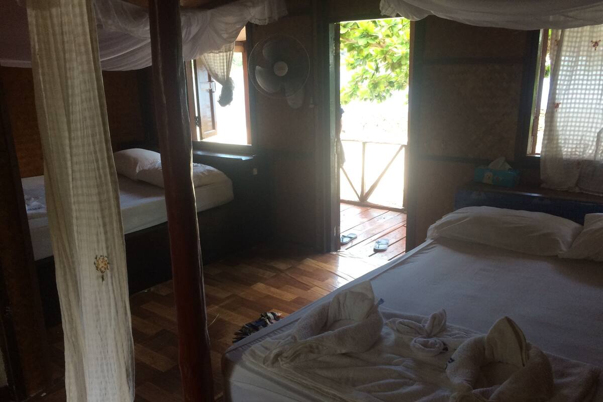 Een slaapkamer met een bed, een raam, een ventilator en een houten vloer.