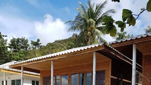 Una cabaña de madera con un porche, ventanas grandes y una playa de arena al frente.
