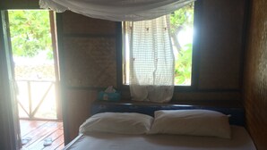 Una cama con ropa blanca, una ventana con cortinas traslúcidas y un piso de madera.