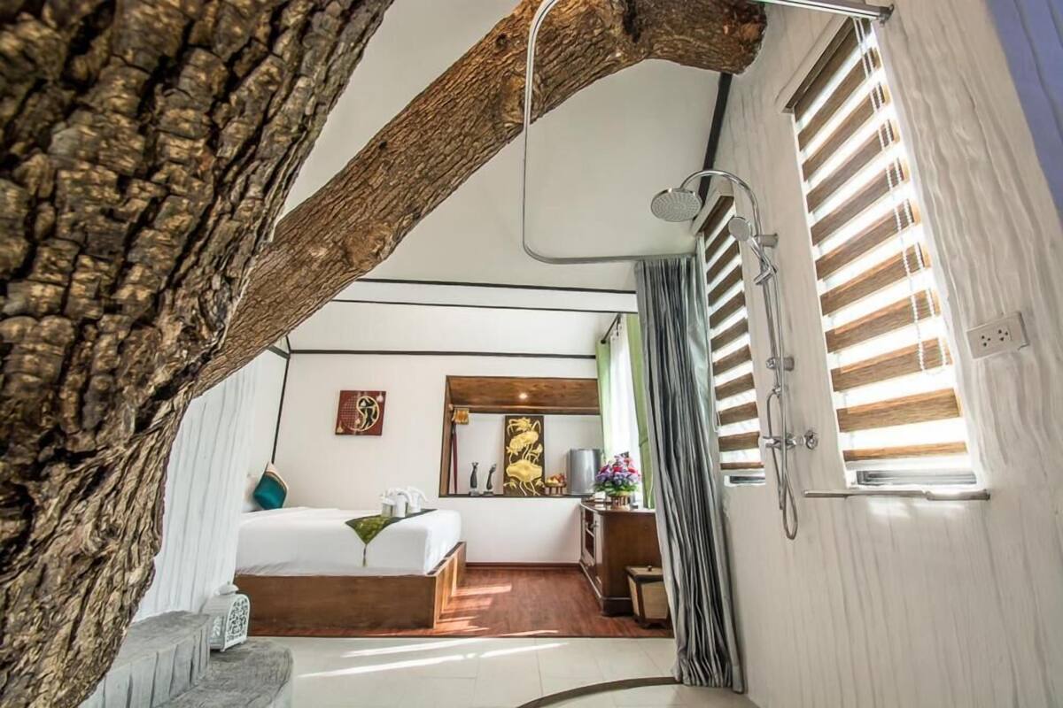A bedroom with a large bed, a mirror, a desk, and a window with blinds.