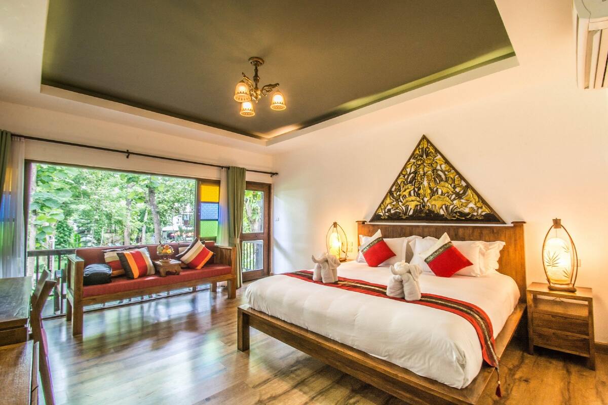 A spacious bedroom with a large bed, a wooden bench, and a view of lush greenery outside.