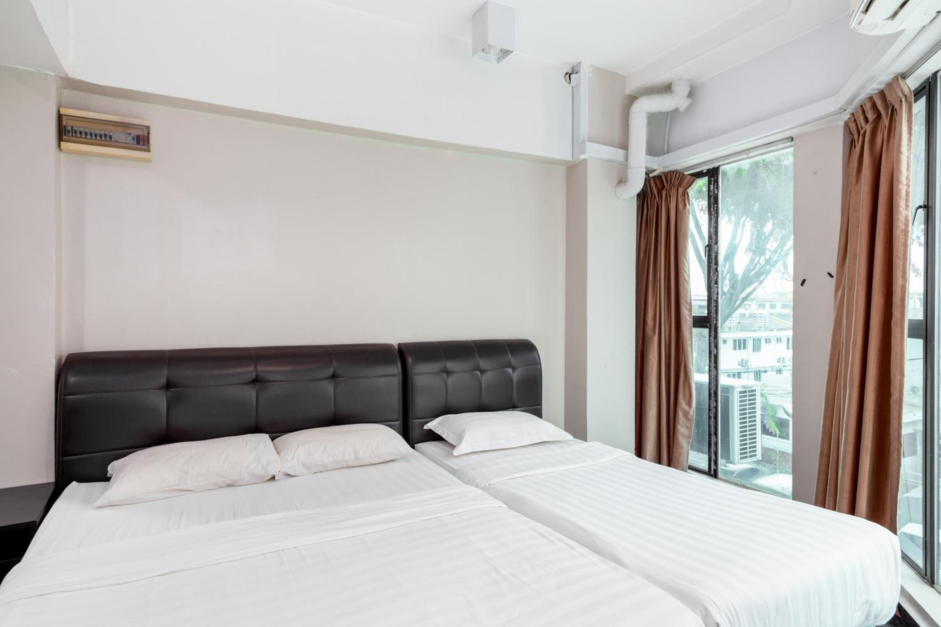 Habitación de hotel con una cama grande, cabecera, ventana con cortinas y un equipo de aire acondicionado.